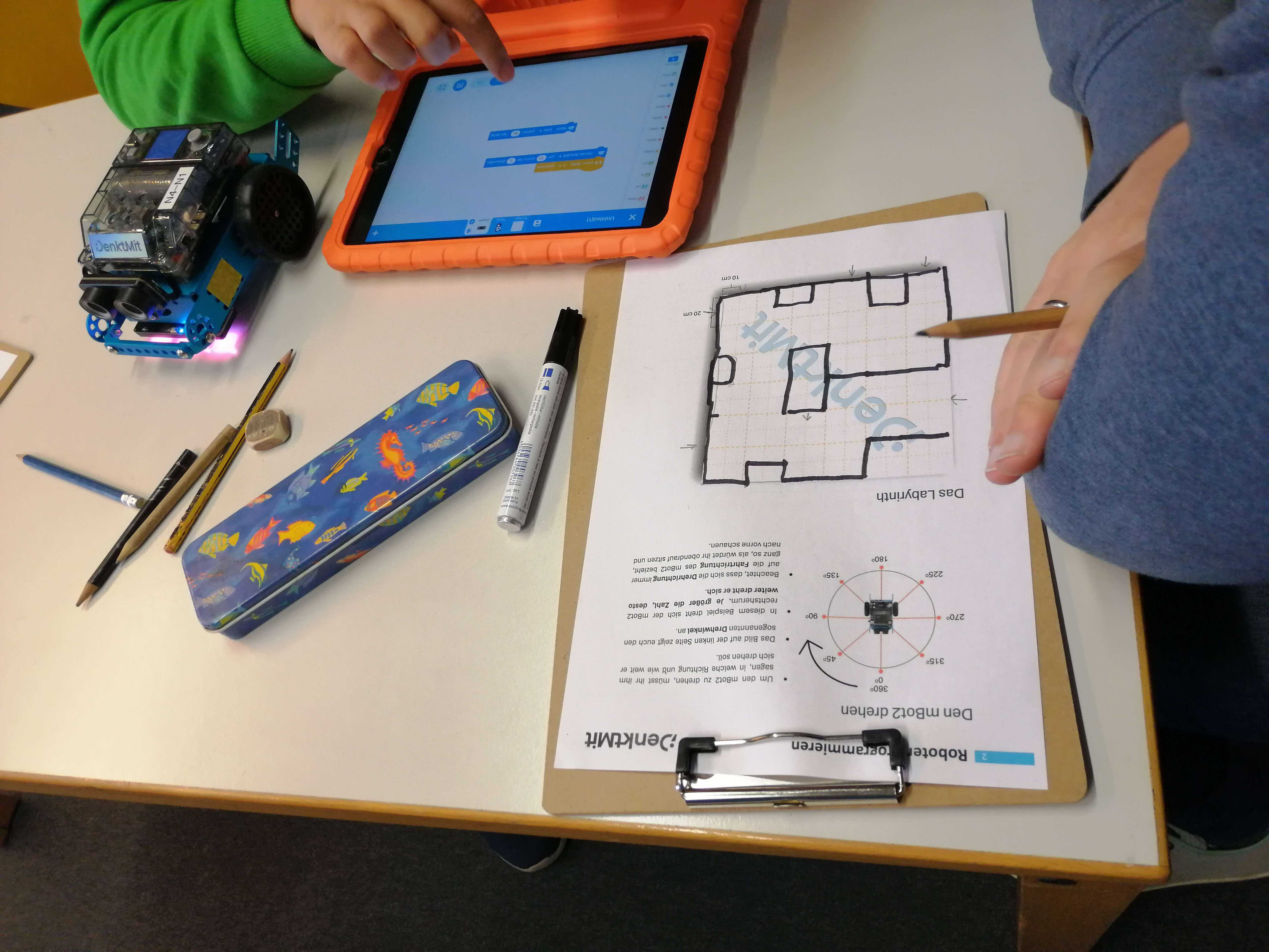 Tisch mit iPad, Unterlagen, Stiften und einem mBot2 Lernroboter