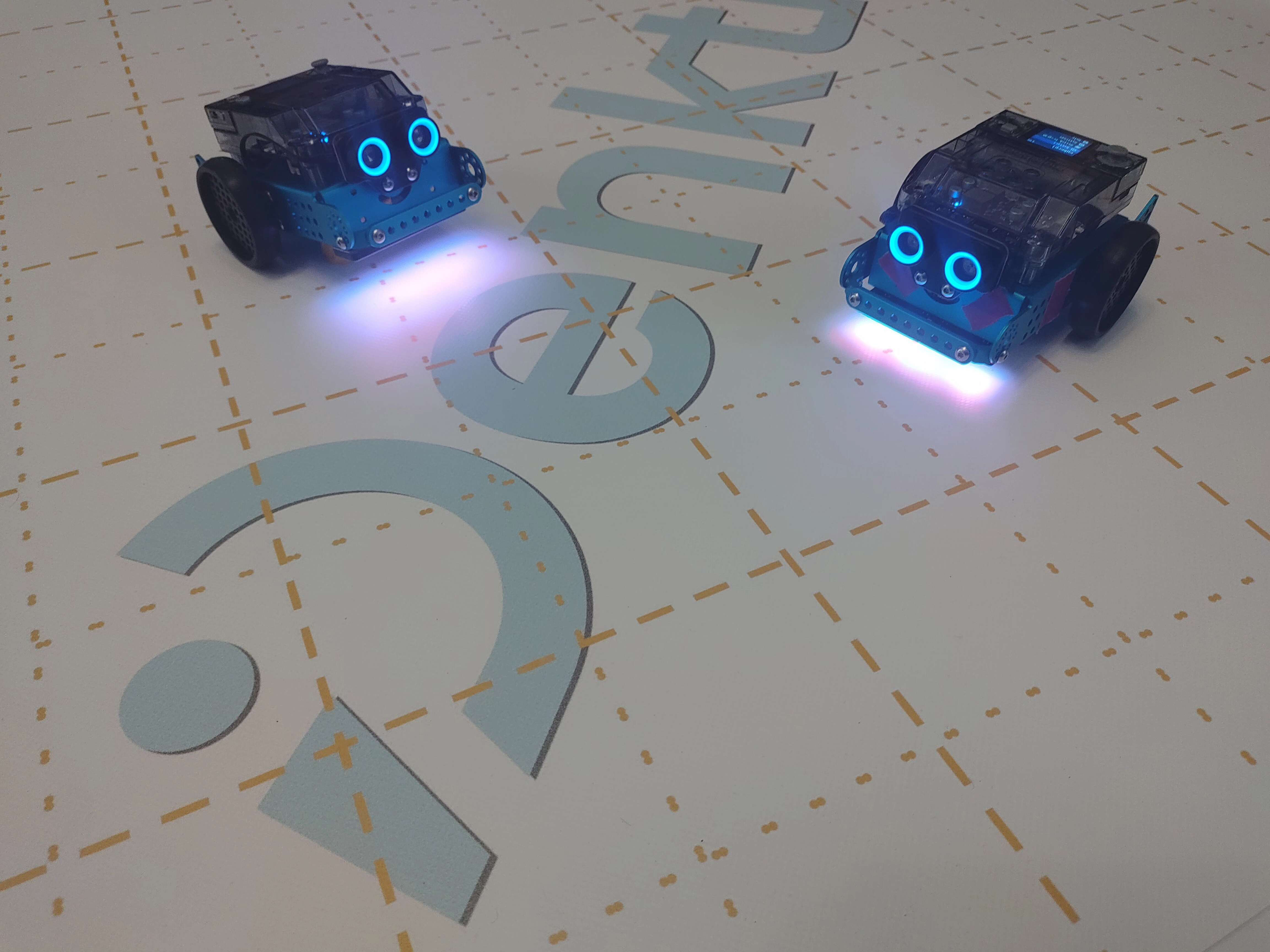 Zwei mBot2 Lernroboter auf einer PVC Matte mit DenktMit-Logo